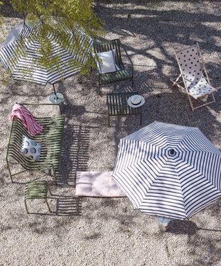 A gravel space with elegant metal furniture and striped parasol to answer how much does a patio cost.