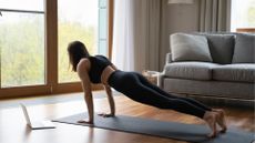 white girl facing away from camera wearing black leggings crop top plank position laptop sofa living room 