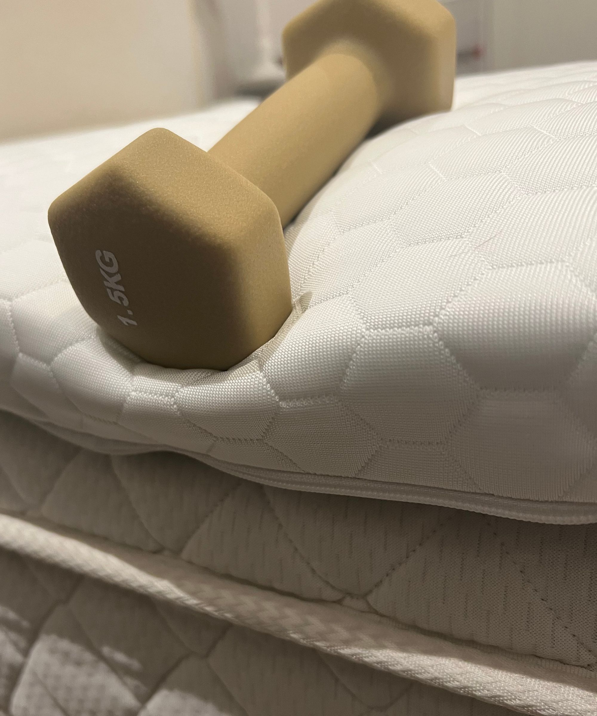 Testing the Nolah mattress topper edge support with a brown dumbbell, on top of a white mattress.