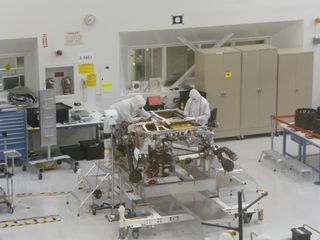 Technicians at NASA's Jet Propulsion Laboratory work on the Mars Science Laboratory rover Curiosity in May 2011. The rover is upside-down, and its six wheels are off (they rest on a table, at far right of the photo).