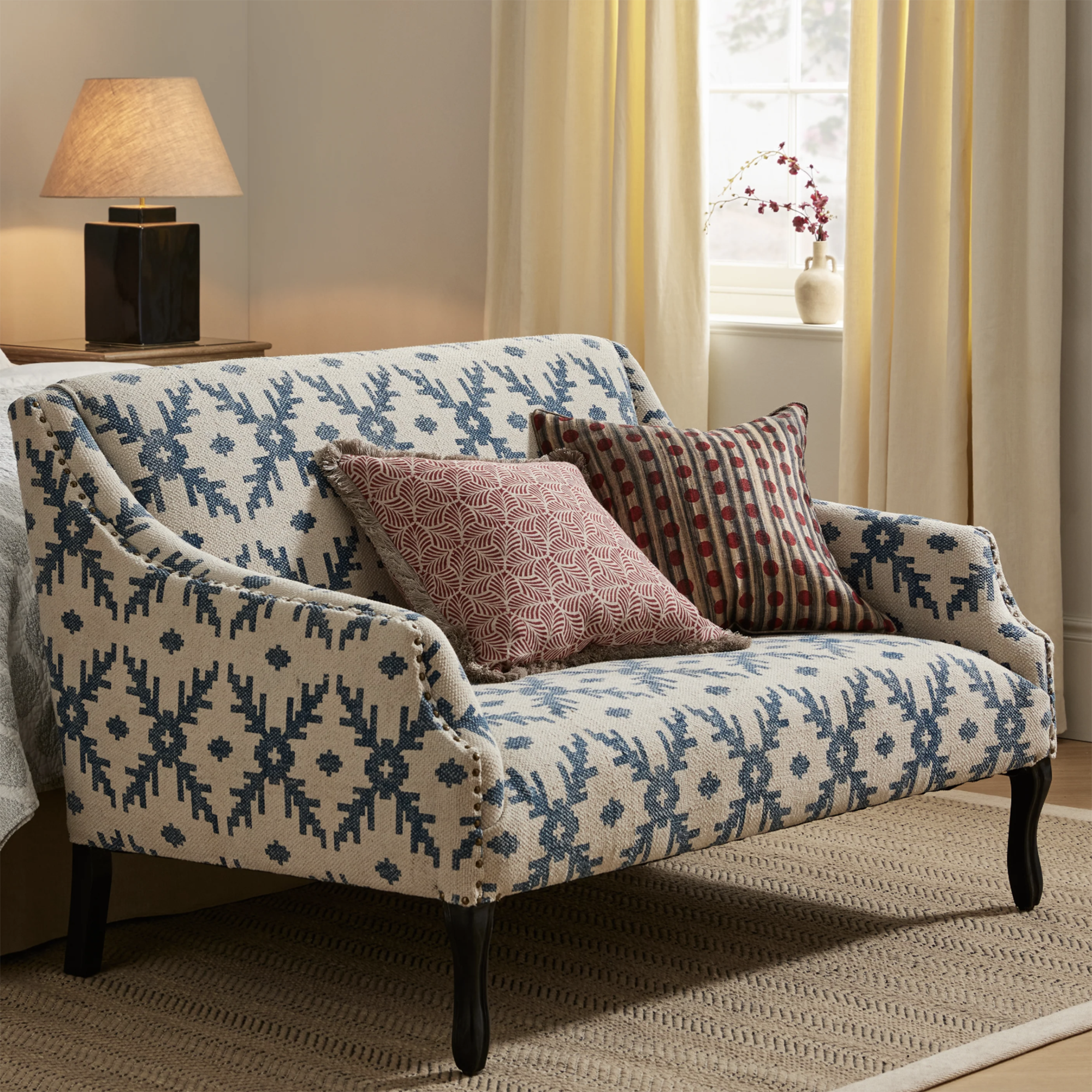 blue patterned sofa with red cushions at the end of a white bed