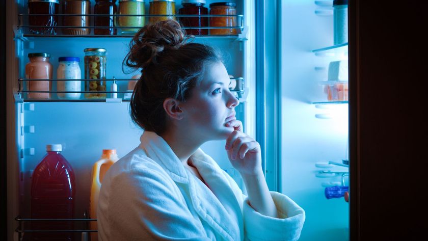 A woman looking inside a fridge to decide what to eat as a nighttime snack