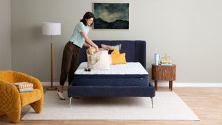 A brunette women looks through a beige handbag that rests on the new Serta Five Star Mattress in a clean, well-lit bedroom.