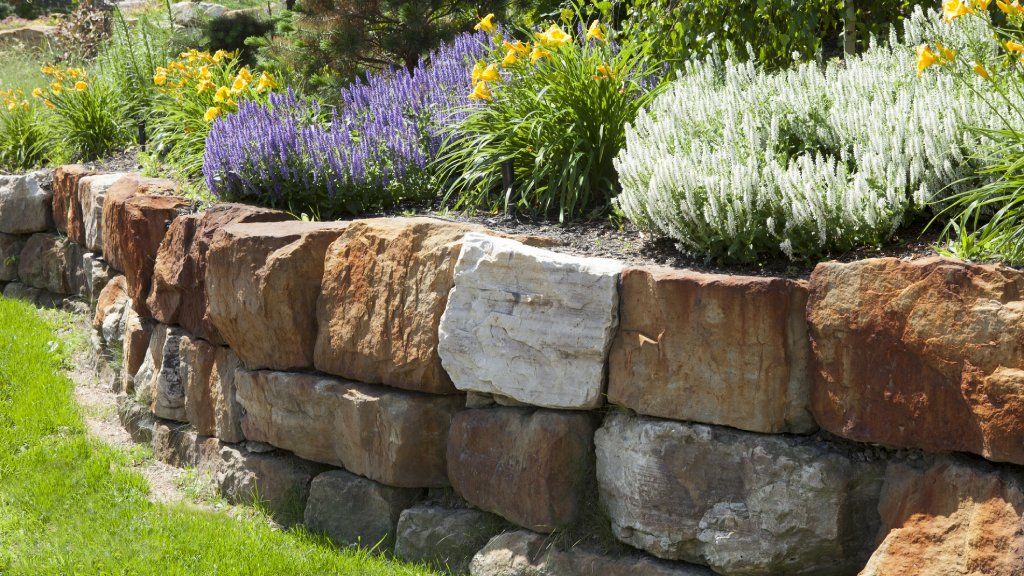 A stone retaining wall along a flower garden