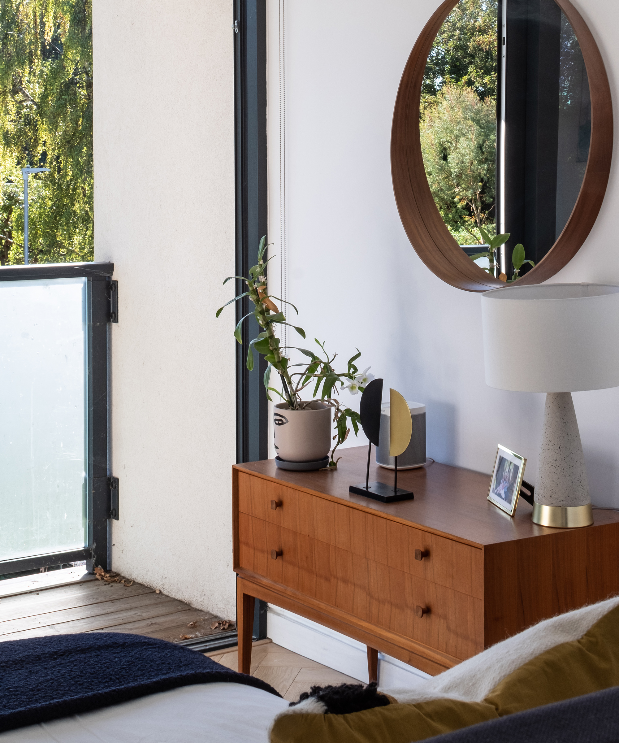 A wooden bedside table with a variety of modern ornaments and lamp