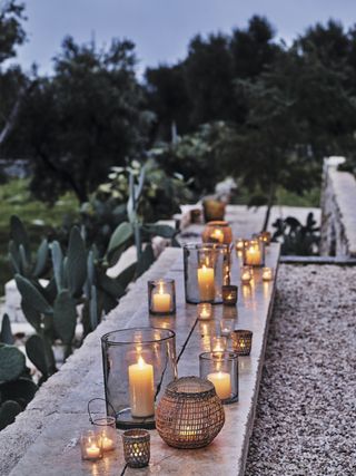 Storage jars and seagrass candle holders filled with pillar candles to create striking outdoor lighting feature by the white company
