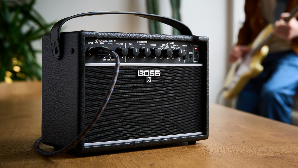 Boss&#039;s new Katana-Mini X amp sits on a table in a room as a guitarist plays through it