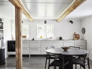The light-filled kitchen inside the Vipp Farmhouse with a sleek grey aluminium kitchen, round black table and original wooden columns
