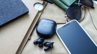 Bose QuietComfort Earbuds 2 ligger utanför sitt fodral bredvid en iPhone och lite andra prylar.