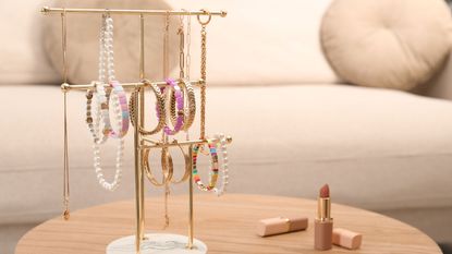 A necklace standing holding necklaces and bracelets nect to an open tube of nude lipstick