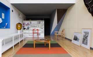 A room with book shelf, frames and furniture with coloured carpet