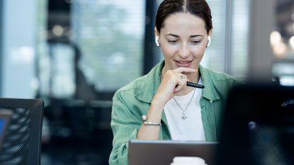 A woman appears intrigued as she looks at her laptop screen in an office.