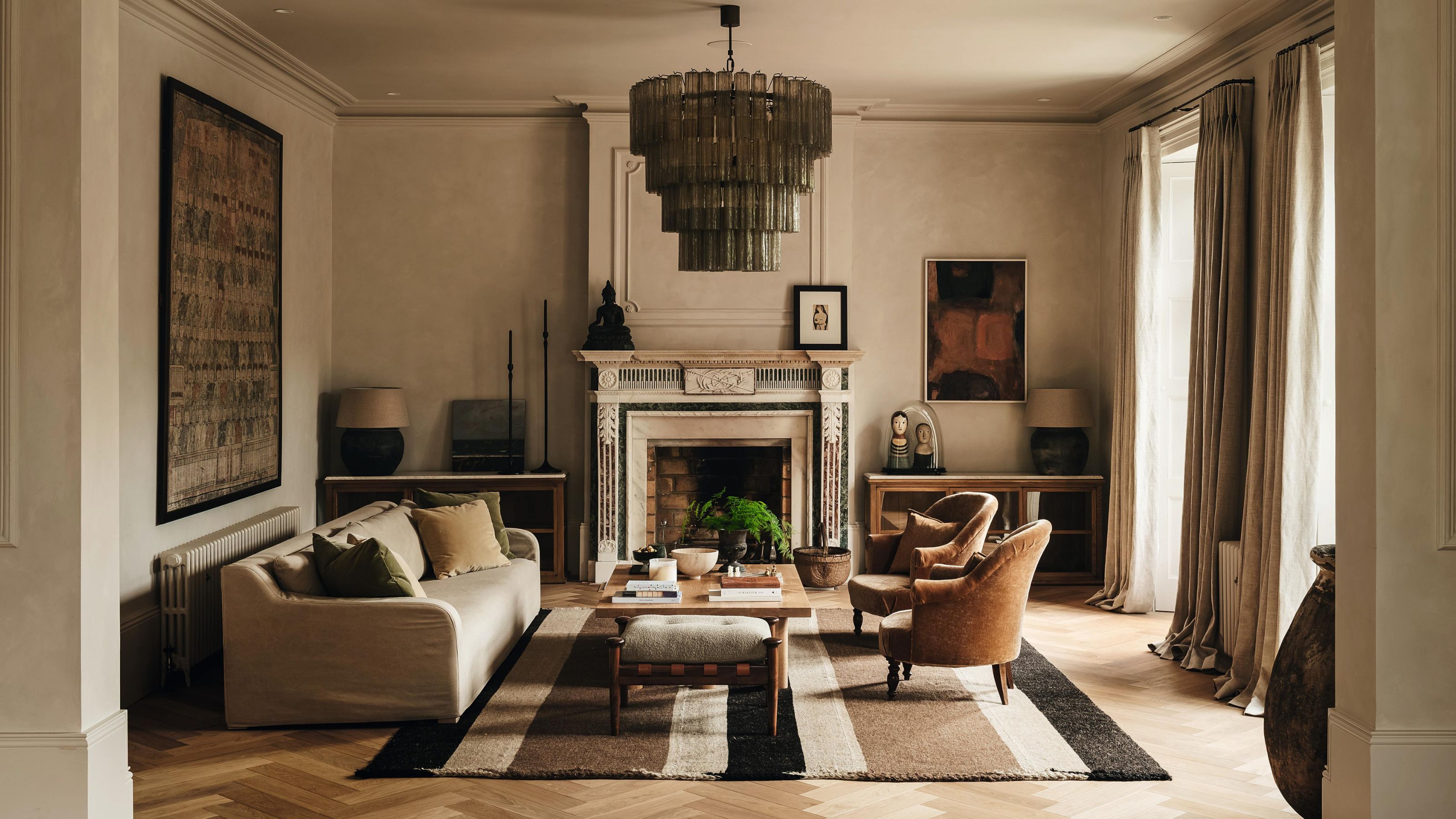 an earthy victorian living room in England with a large green glass chandelier, victorian fireplace, striped rug, and neutral furnishings
