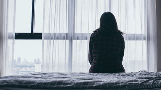 A woman in silhouette sitting on a bed looking out the window