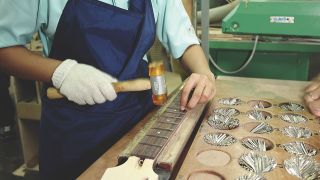 A woman hammers frets in an Indonesian guitar factory