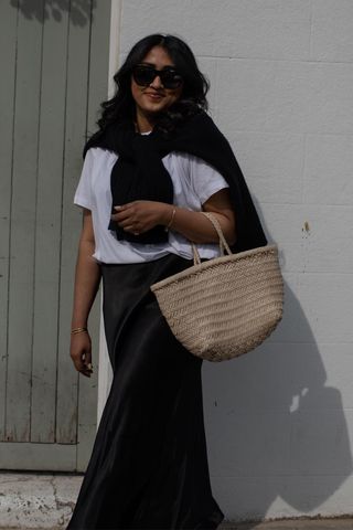 a photo of a woman's spring vacation outfit with a white t-shirt, black slip skirt, tied cardigan and raffia bag