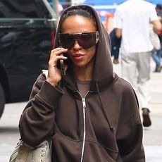 FKA Twigs wearing a brown hoodie, brown Bermuda shorts, brown boots, a gray shoulder bag 