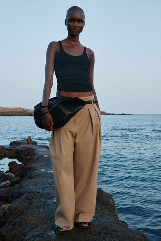 Model wears Wide Belted Pants while standing on rock by the water