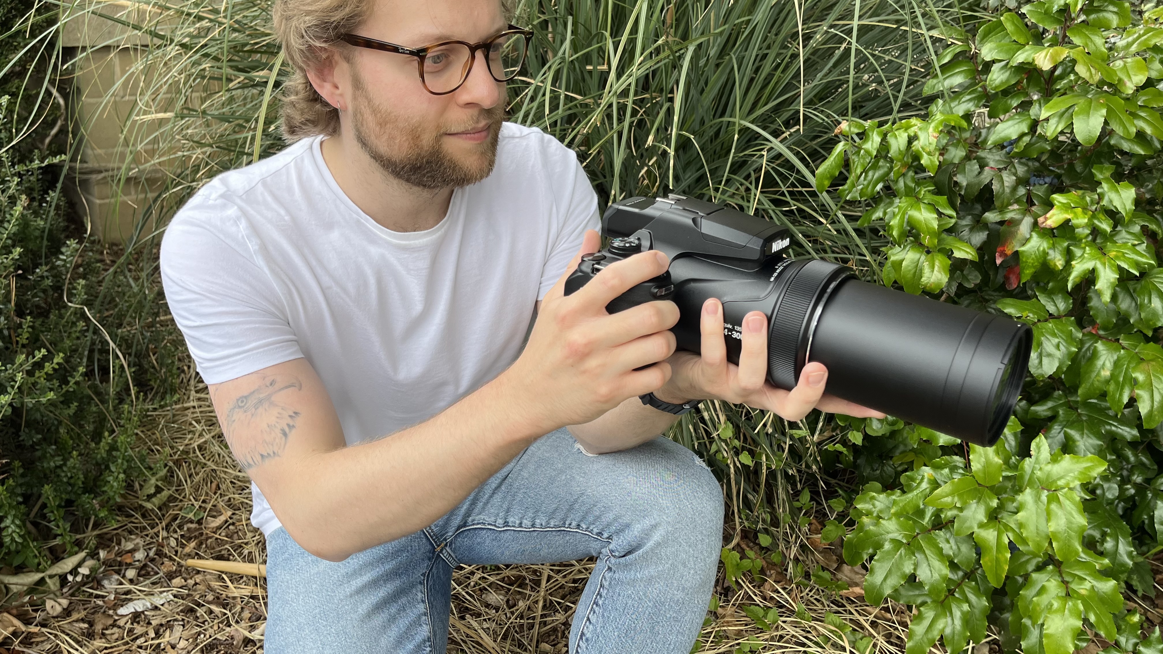 Nikon Coolpix P1100 lifestyle image of crouching Mike Harris holding P1100 in front of vegetation
