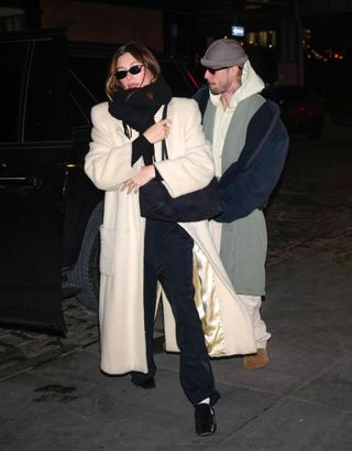 A photo of Hailey Bieber accessorizing her beige brushed wool coat with a black scarf and bag from The Row.