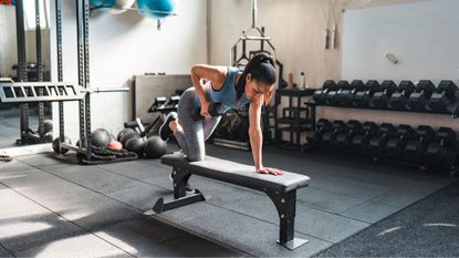Woman doing single arm dumbbell rows on bench in the gym