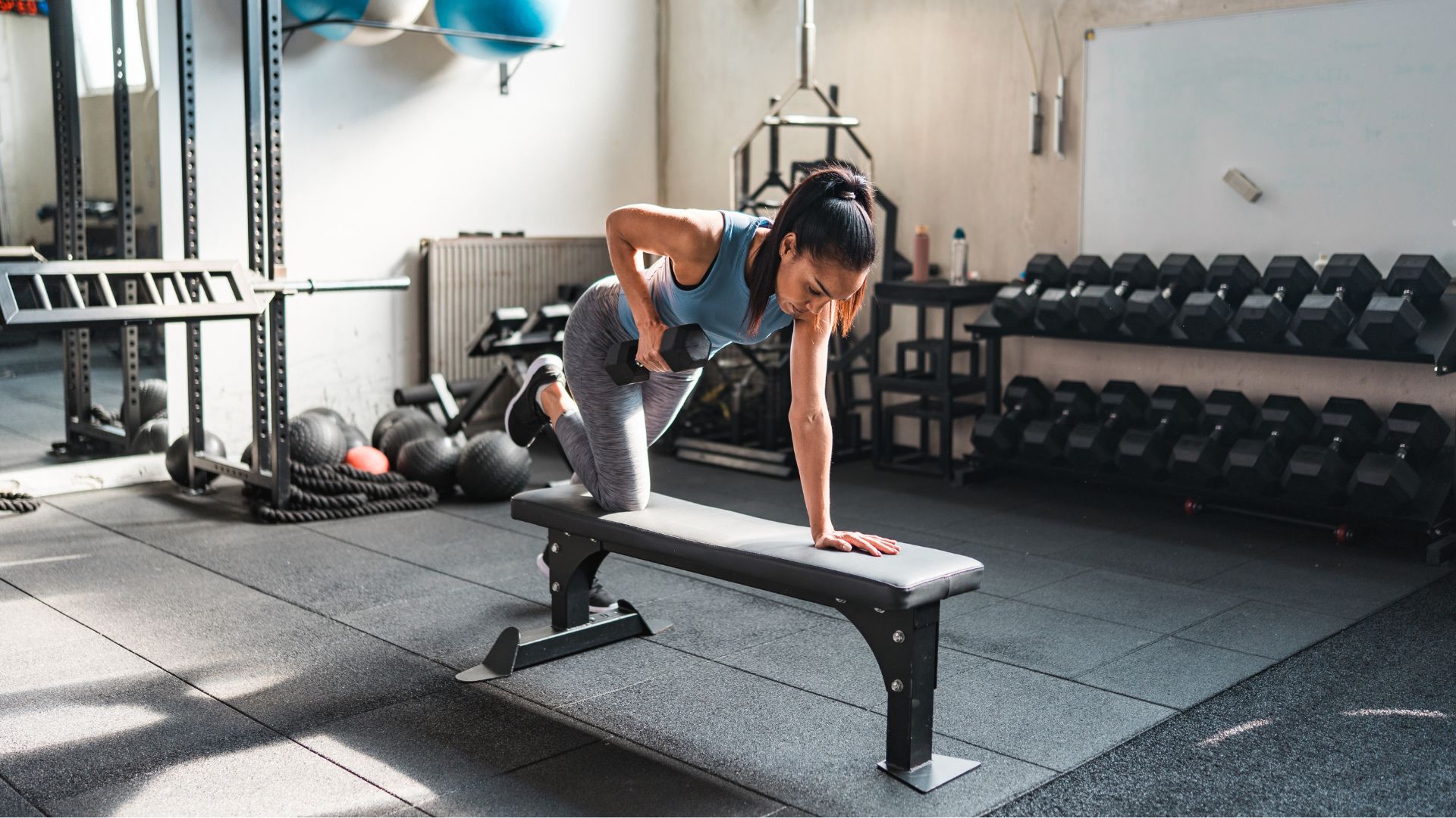 Woman doing single arm dumbbell rows on bench in the gym