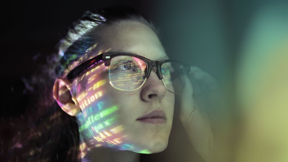 Female software developer using GitHub Copilot AI assistant on computer station with screen reflection in her spectacles.