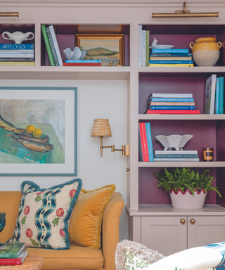 pink and purple bookshelves and sofa with artwork on wall and plant and books and ceramics and mustard sofa