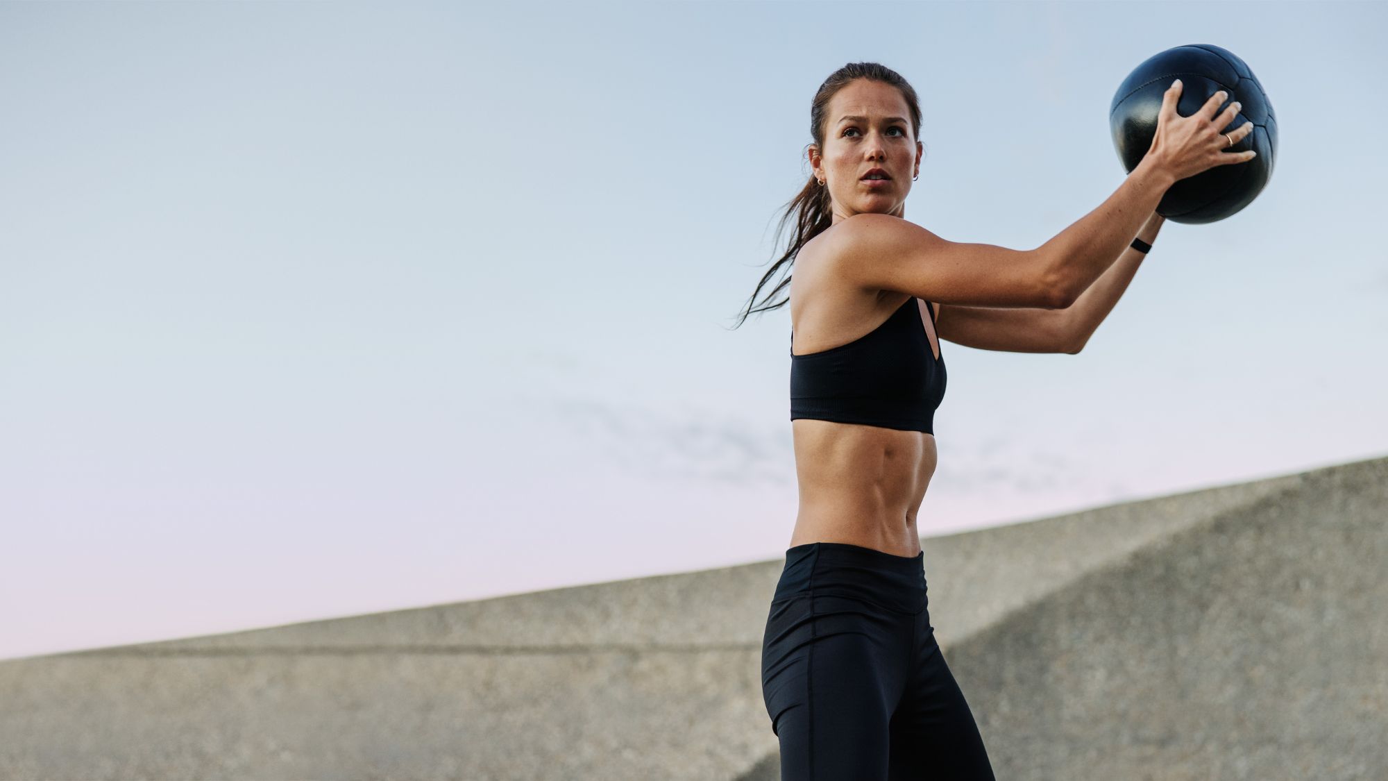 A woman throwing a medicine ball against a wall: Strength training in an outdoor gym