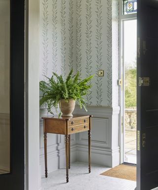 entrance with marble herringbone floor tiles leaf wallpaper, light gray panelling and small wooden chest of drawers