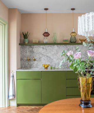 Green kitchen cabinets with peach walls and marble splashback