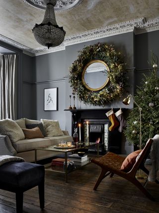 Christmas living room with wreath around mantel mirror, stockings, tree, candles, neutrals sofa, armchair, coffee table and footstool, grey walls