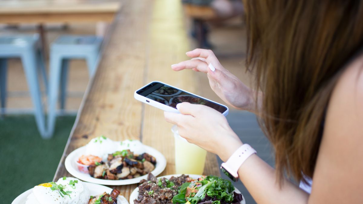 A photo of a person taking a photo of plates of food using an iPhone in a white case