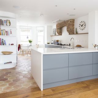 kitchen with white and blue cupboards, brown hexagonal foor tiles, white corner in-built display shelves and a brick arch feature above the stove