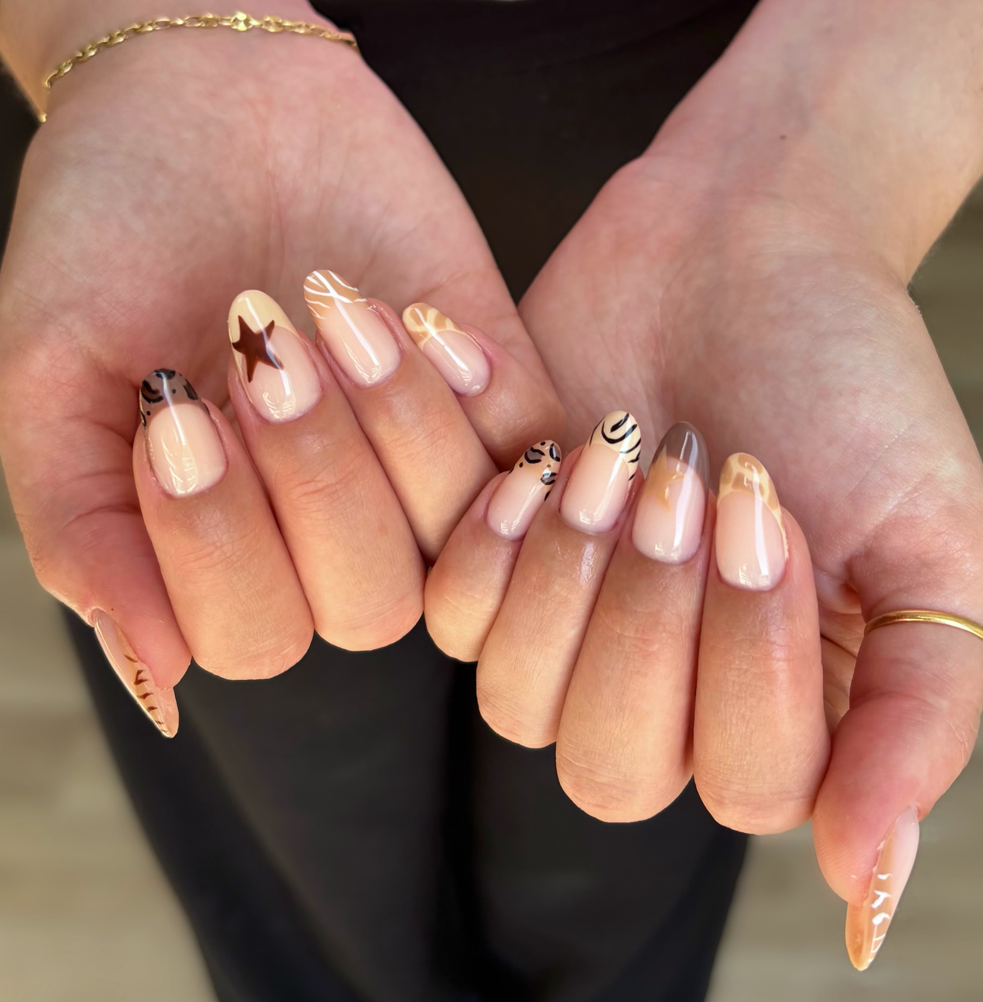 almond nails with brown, black, cream and taupe stars, animal stripes, and abstract shapes over a sheer pink base