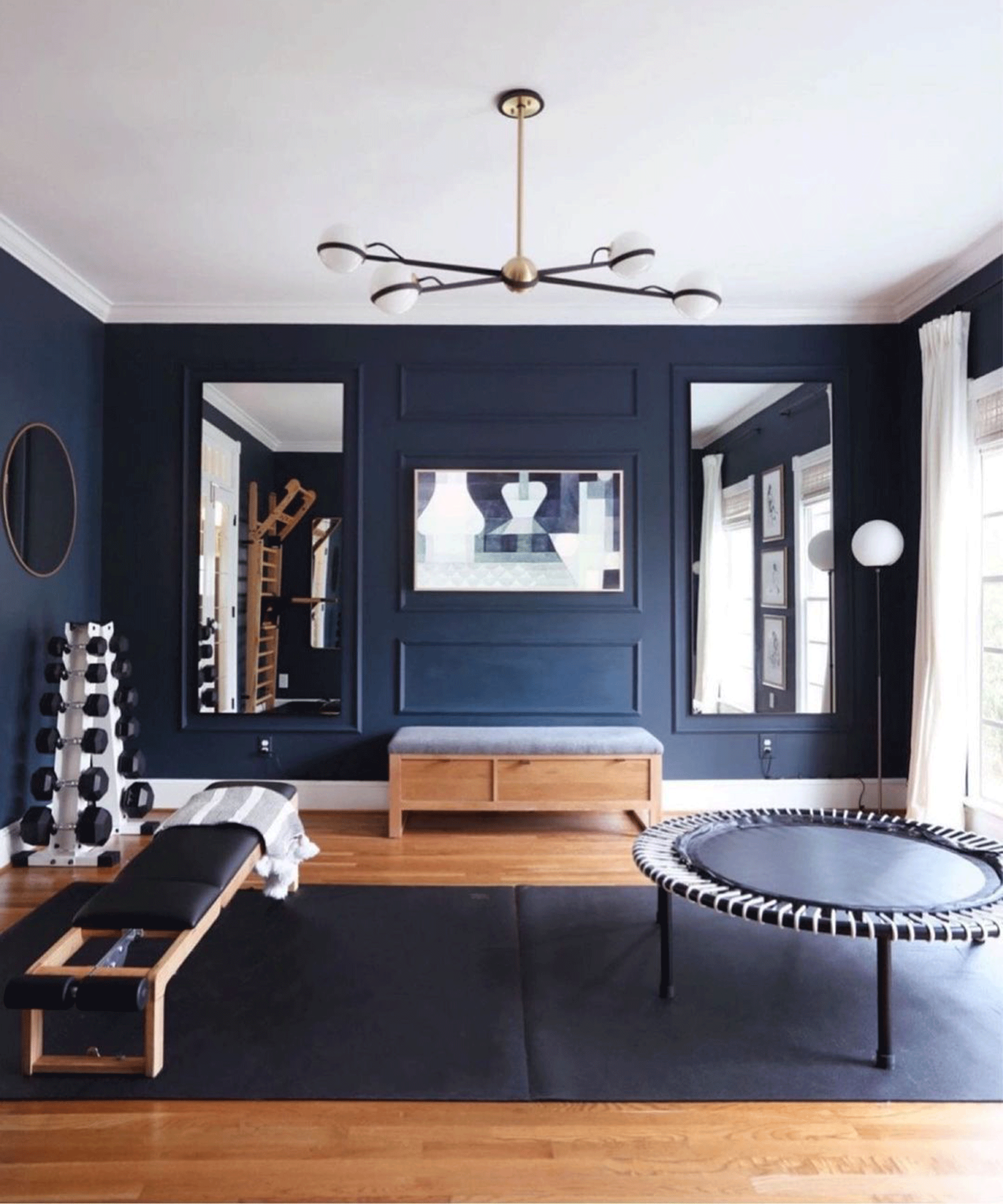 A modern dark blue gym with two wall-hung mirrors, trampoline and free weights