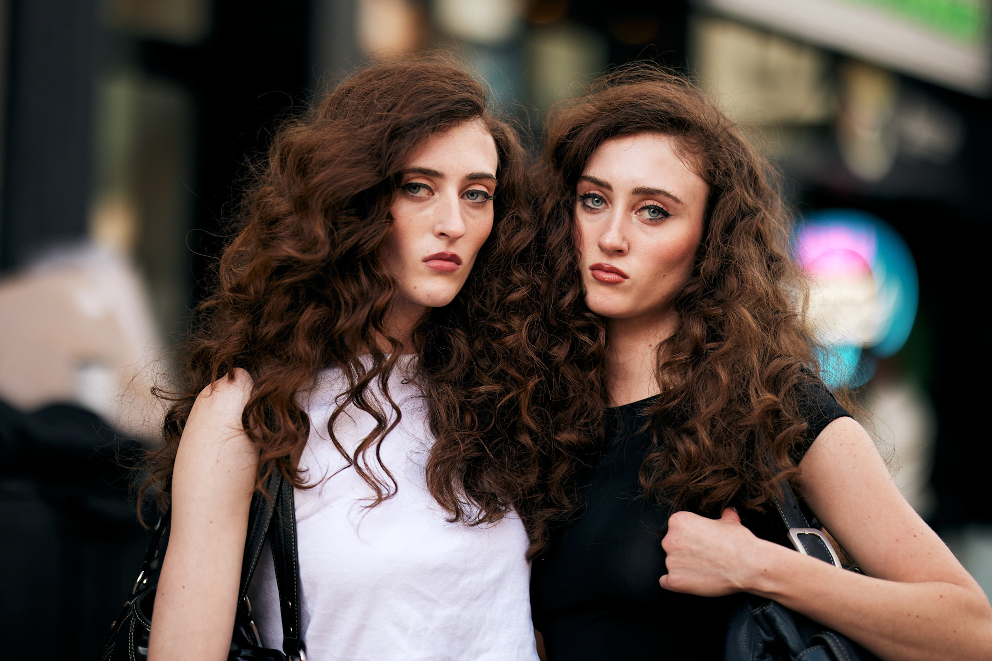 two women with brunette curly hair, and one is wearing a black t-shirt, the other is wearing a white t-shirt
