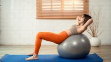 Woman laying on her back on a Stability ball with hands behind head and feet on exercise mat