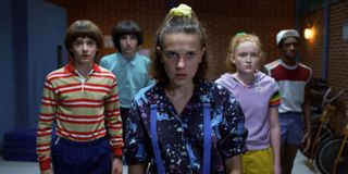 a group of kids led by millie bobby brown as eleven in 80s clothing in a still from stranger things