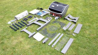 The parts of the Weber Spirit II E-310 laid out on a lawn, ready to be assembled