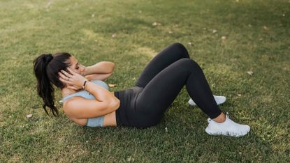 Woman completes an ab workout outside on some grass