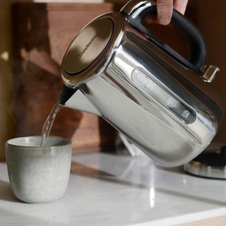 Stainless steel kettle pouring water into grey mug