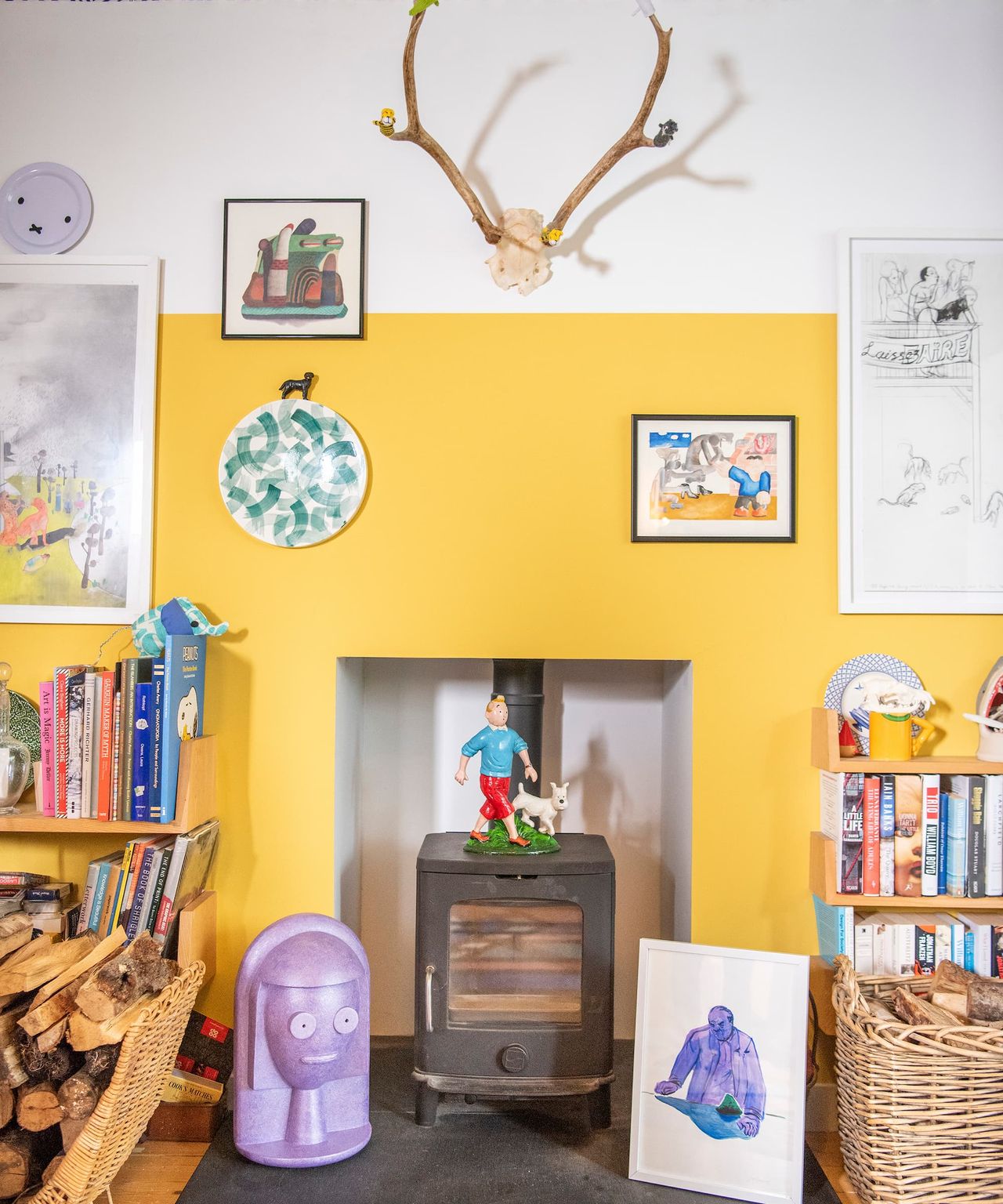A yellow wall behind a central fireplace with antlers hanging above it