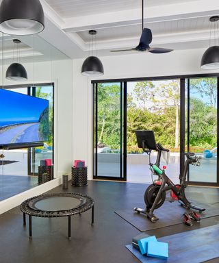 Home gym with black floor, TV, mini trampoline, exercise bike, mats, storage for mats, and doors to terrace beyond