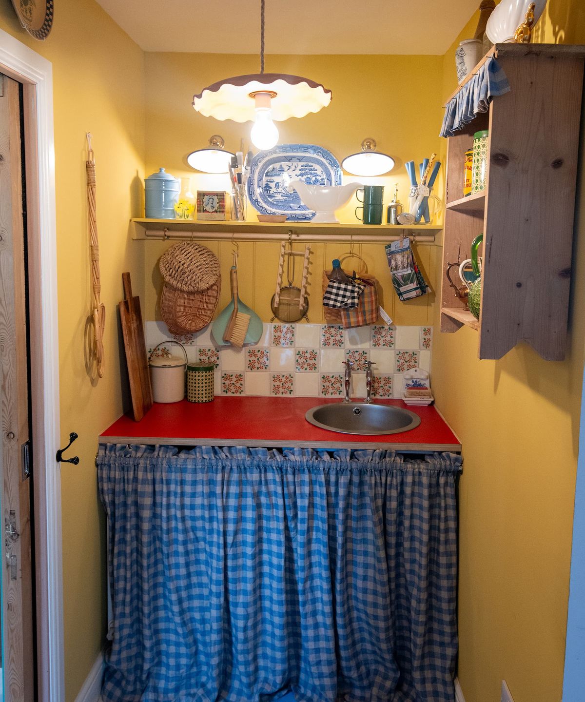 A kitchen sink with a curtain covering the pipework and handmade cupboard