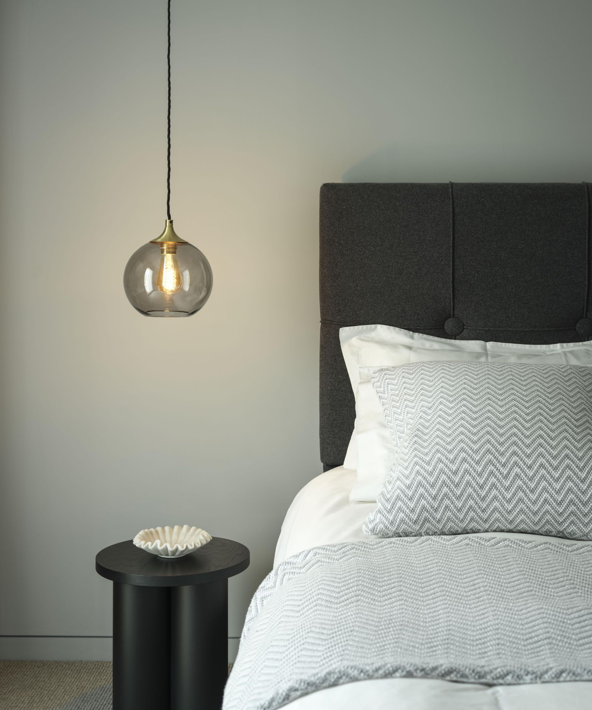 Minimal bedroom with chevron throw and matching pillow, black round side table and hanging glass pendant light