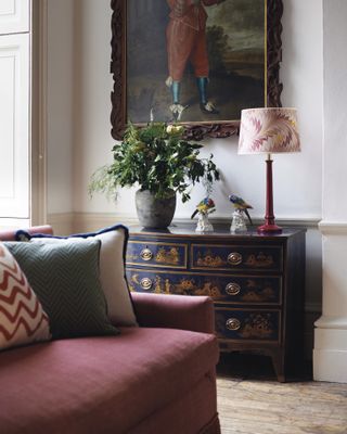 A navy and gold vintage chest of drawers next to a red sofa and oil painting.