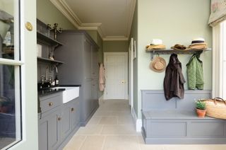 A large mudroom with gray cabinets and a gray wooden bench below coat hooks