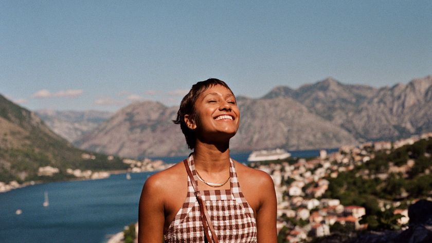 Smiling young woman enjoying sunlight against mountain range and sea during vacation.
