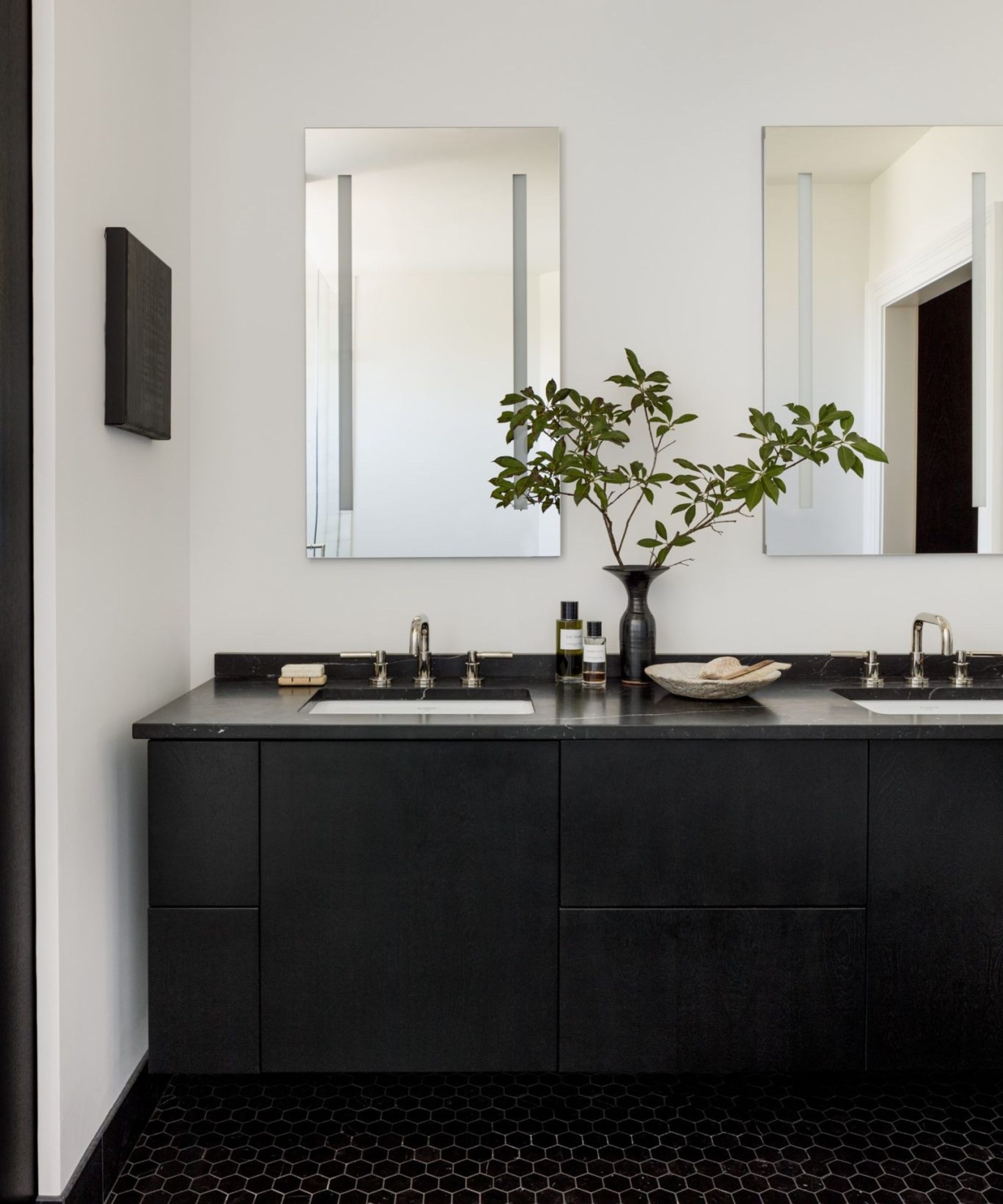 A minimalist bathroom with white walls, chrome hardware, a black vanity, and black tiled floor